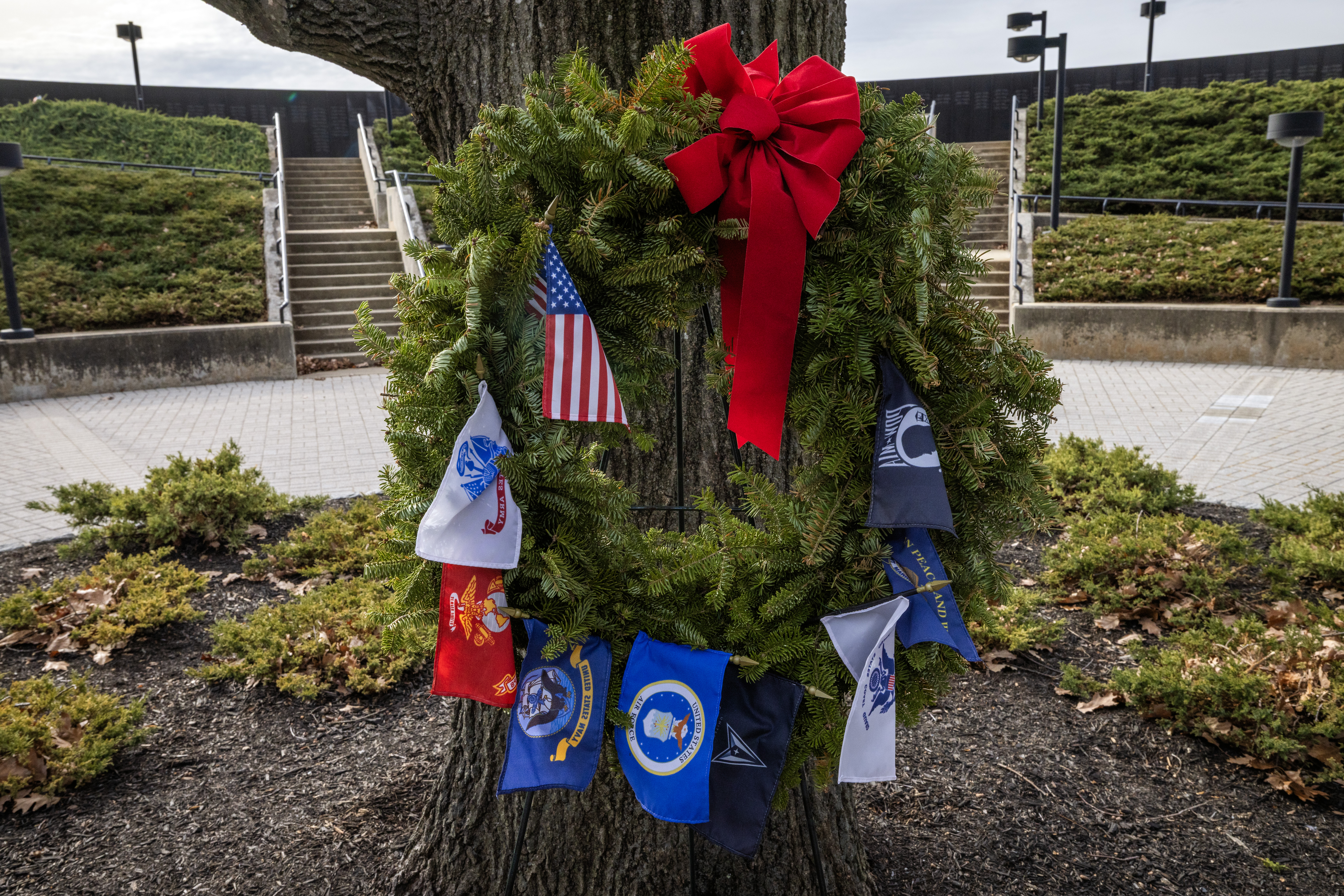 A wreath with all service flags is placed at the base of the Northern Red Oak, New Jersey’s State Tree, at the New Jersey Vietnam Veterans Memorial in Holmdel, New Jersey, Dec. 10, 2025. Wreaths were placed at the base of each of the memorial’s 366 eight-foot-tall black granite panels – each representing a day of the year – listing the names of the 1,564 New Jersey men and one woman who gave their lives while serving in Southeast Asia. In addition, the Wreaths Across America convoy stopped at the memorial on their annual journey to Arlington National Cemetery. This year marks the 50th anniversary of the end of the Vietnam War. (New Jersey Department of Military and Veterans Affairs photo by Mark C. Olsen)
