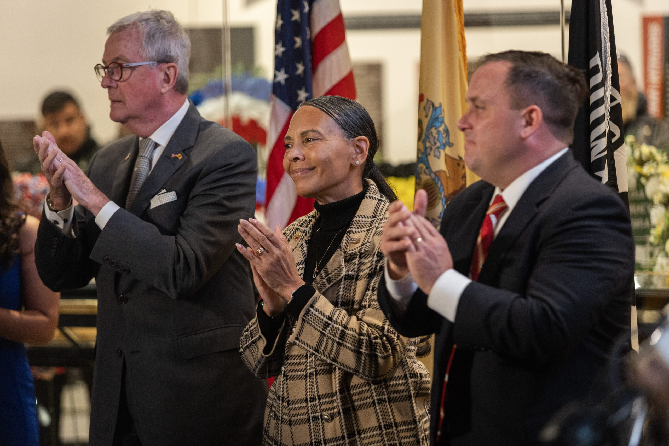 New Jersey Gov. Philip D. Murphy, left, Brig. Gen. Yvonne L. Mays, center, The Adjutant General of New Jersey, and Vincent Solomeno III, Deputy Commissioner of Veterans Affairs, New Jersey Department of Military and Veterans Affairs, and Administrator of Veterans Affairs for the State of New Jersey applaud during the invocation at the State Veterans Day ceremony at the New Jersey Vietnam Veterans’ Memorial, Vietnam Era Museum and Educational Center at Holmdel, New Jersey, Nov. 11, 2025. Veterans Day celebrates and honors America’s veterans for their patriotism, love of country, and willingness to serve and sacrifice for the common good. (New Jersey Department of Military and Veterans Affairs photo by Mark C. Olsen)